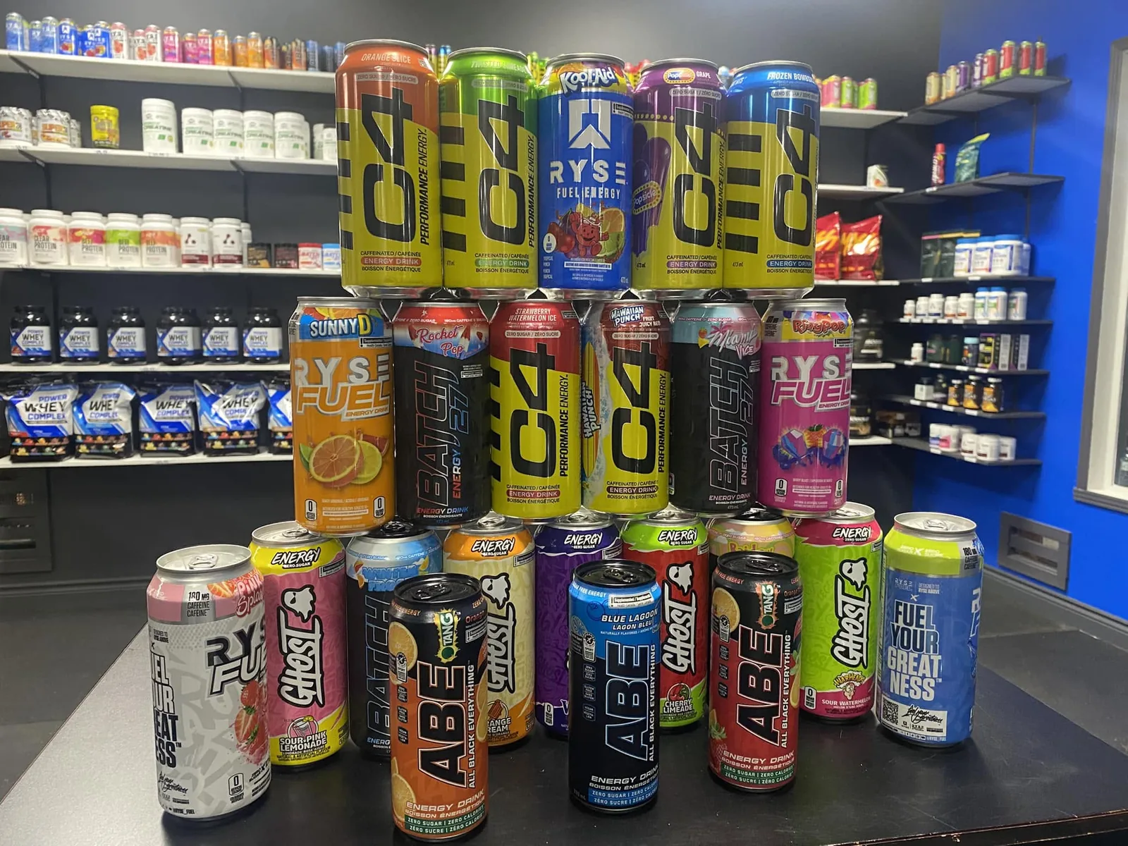 Pyramide de canettes de boissons énergisantes devant les rayons de protéines du comptoir Popeye’s Suppléments